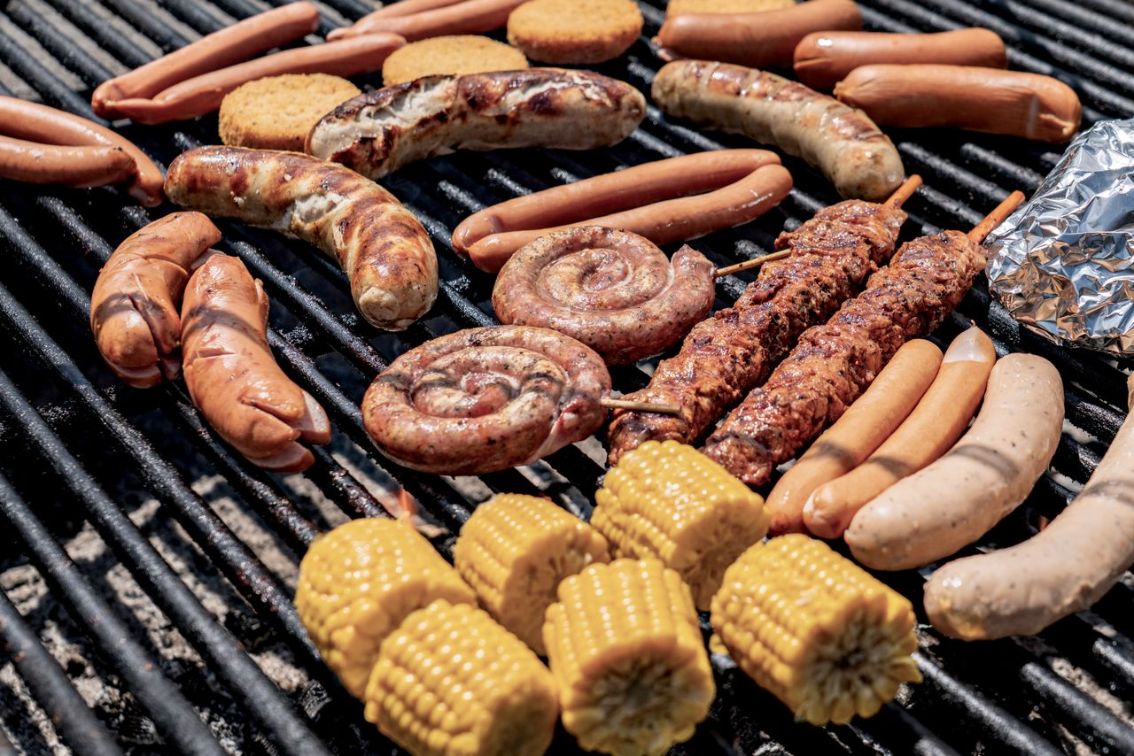 Delicious variety of meats and corn grilling outdoors on a barbecue.